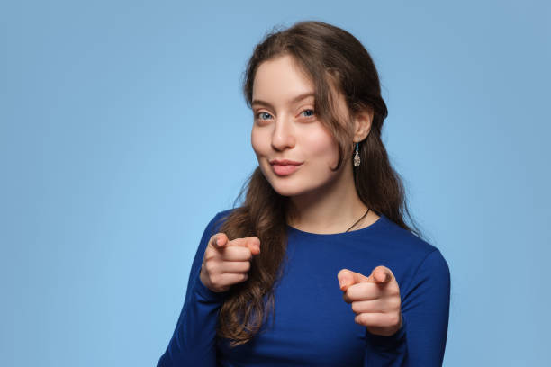 Young lady looking and pointing her index fingers at the camera. Long hair, blue eyes, and blue clothes. stock photo