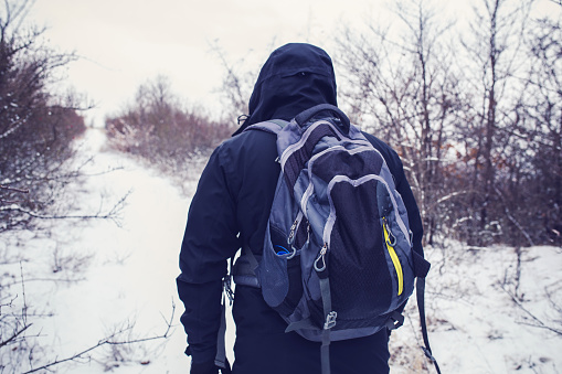 Hiker with backpack walking on snowy road through forest