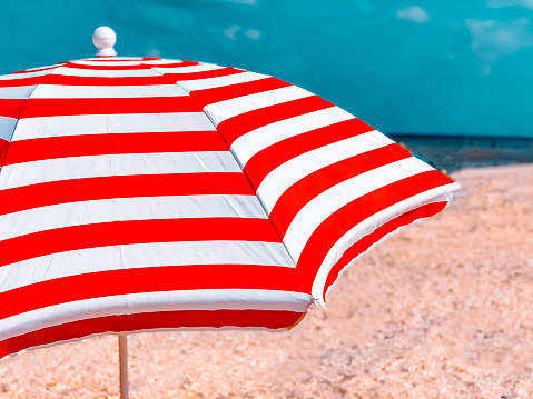 Part of a striped beach umbrella against a beautiful blue sky, side view. Tourism and summer vacation concept.