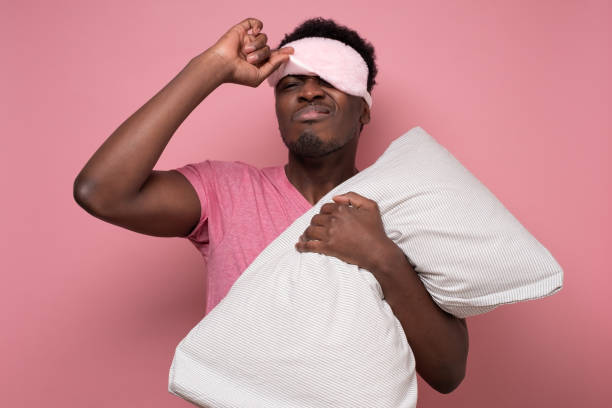 istock Man yawning waking up, holding pillow in hands, taking off his blindfold. 1302160347