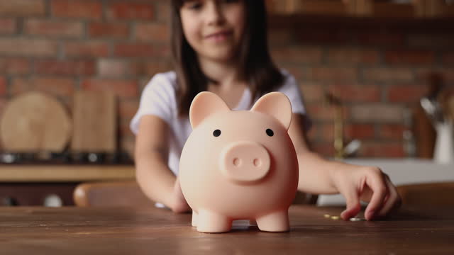 Little girl putting coin into piggy bank, close up