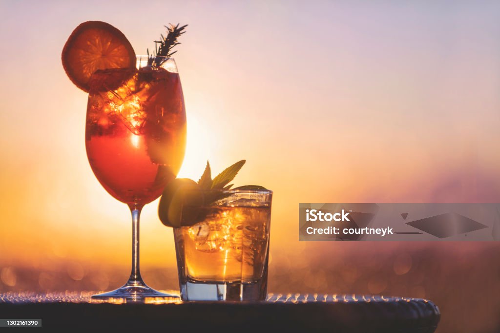 Two cocktails at sunset. Two cocktails at sunset. One is a spritz with orange, the other is a mojito with mint and lime. The sun and sky is behind them Cocktail Stock Photo