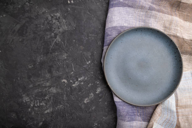 istock Empty blue ceramic plate on black concrete background and linen textile. Top view, copy space, flat lay. 1302162389