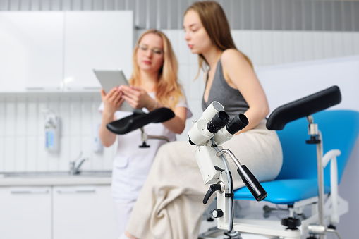 primer plano del colposcopio sobre el fondo de una imagen borrosa de un ginecólogo y un paciente en una silla ginecológica azul. photo