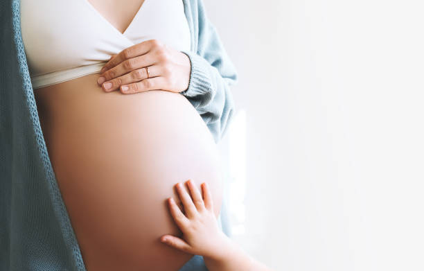 concepto de familia, embarazo, maternidad, nueva vida. primer plano hermosa mujer embarazada vientre con la mano y la mano del niño pequeño. - second skin fotografías e imágenes de stock