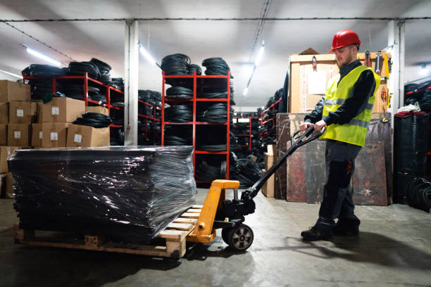 istock Young male worker with hand pallet jack unloading pallet goods in a warehouse 1302175062