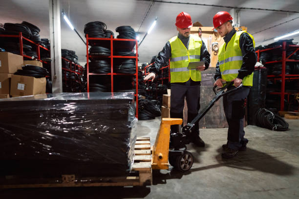 Young male workers sorting finished rubber mats for the gym in a warehouse by using a digital tablet and pallet jack