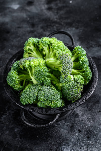 istock Organic Raw green broccoli cabbage  in a colander. Black background. Top view 1302178836