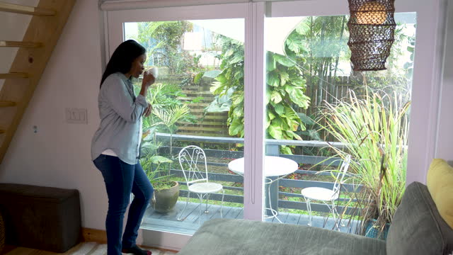 Mature black woman drinking coffee by patio doors