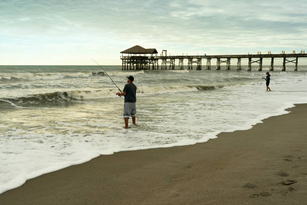 Florida, USA - January 3, 2021: A Hispanic man and his daughter stand in water to fish at Cocoa Beach Pier.
