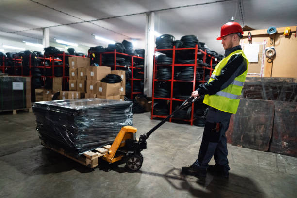 istock Warehouse worker with hand pallet jack unloading pallet goods in a warehouse 1302187836