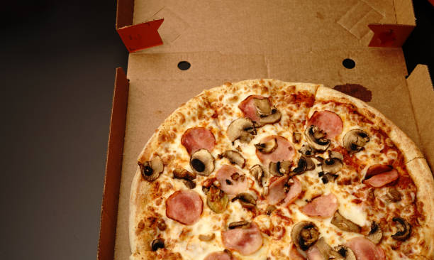 istock Pizza in a box on a black background. With cheese and mushrooms. Top view. 1302187884