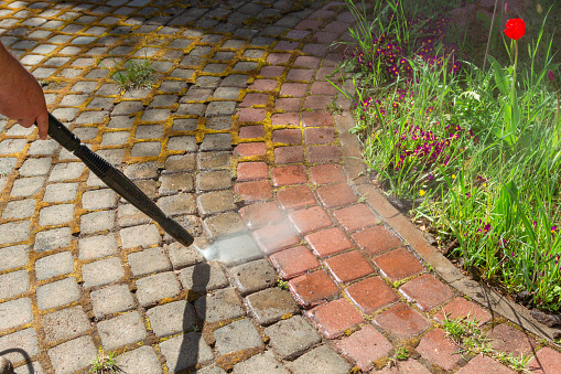 Cleaning street with high pressure power washer, washing stone garden paths.