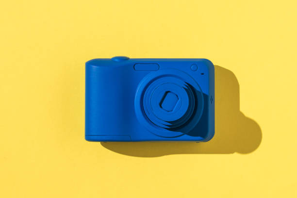 istock Stylish blue camera in bright light on a yellow background. 1302191281