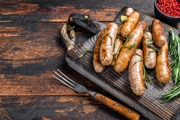 Grilling bavarian sausages on a cutting board. Dark wooden background. Top view. Copy space Grilling bavarian sausages on a cutting board. Dark wooden background. Top view. Copy space. bratwurst stock pictures, royalty-free photos & images