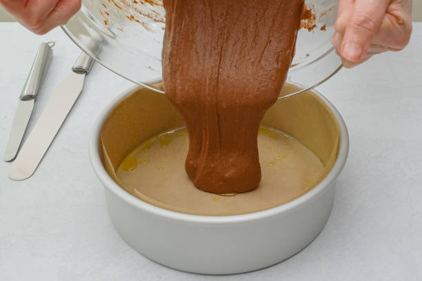 istock Cake pan lined with parchment paper close up on kitchen table, pouring cake batter into the pan. Chocolate cake step by step recipe, close up baking process 1302200990