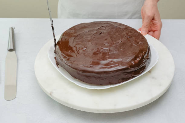 istock Topping chocolate cake with chocolate ganache. Chocolate cake with chocolate cream and chocolate ganache close up on wire rack on kitchen table. Step by step baking process, recipe 1302201061