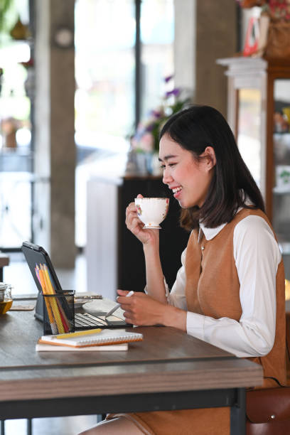 istock Portrait of young female working with computer tablet and drinking hot coffee while sitting in coffee shop. 1302203446