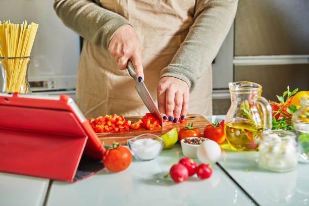 istock Woman cooking according the tutorial of online virtual master class, And looking on the digital recipe, using touchscreen tablet while cooking healthy meal on the kitchen at home 1302206521