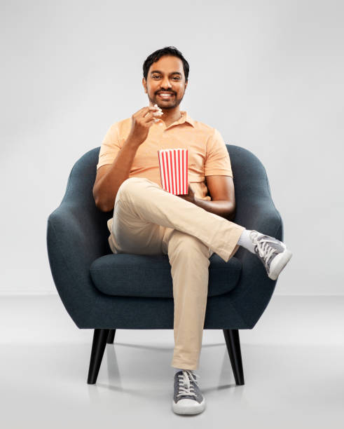 istock happy smiling indian man eating popcorn in chair 1302210207