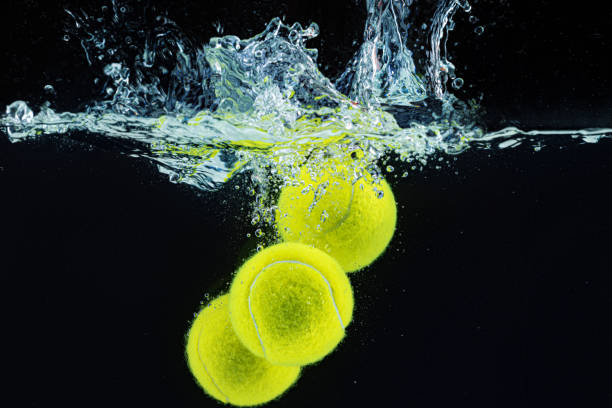 istock Tennis ball falling in water with a splash against dark background 1302213973