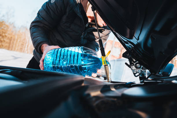 男は車の洗濯機の貯水池に缶から青い不凍液を注ぎます - frost work ストックフォトと画像