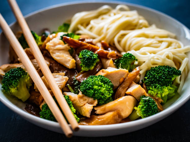 Noodles with chicken nuggets, oyster mushrooms and broccoli on black table