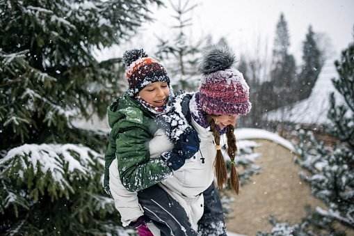 Teenage girl is giving a piggyback ride to her younger brother. Kids are enjoying fresh snow.\nShot with Canon R5