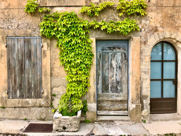 Closeup photo of an old, weathered stone house facade with windows, door and green plants in the popular tourist destination town of Gordes in the south of France.