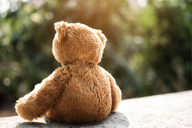 istock Broken heart concept. teddy bear sitting on cement wall. for isolation, loneliness, abandoned child, conceptual. 1302223552