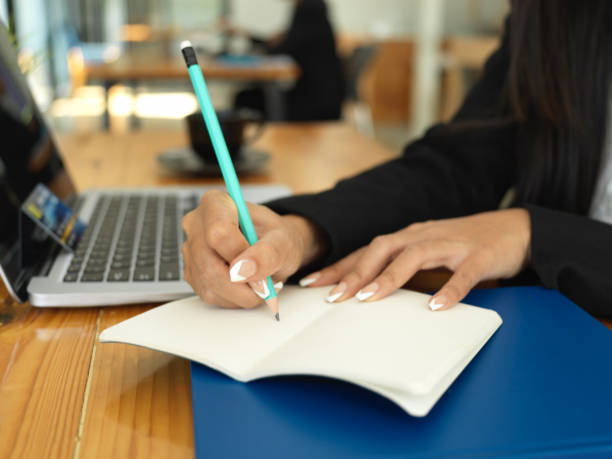 istock Businesswoman hand with pencil writing on notebook while working with laptop 1302227612