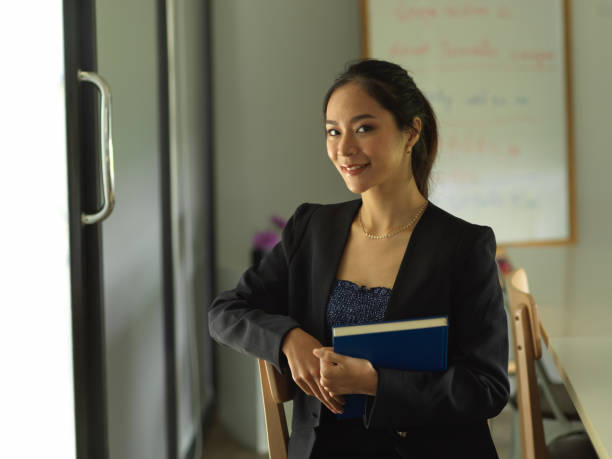 istock Businesswoman smiling to camera and holding textbook while sitting in library 1302227637