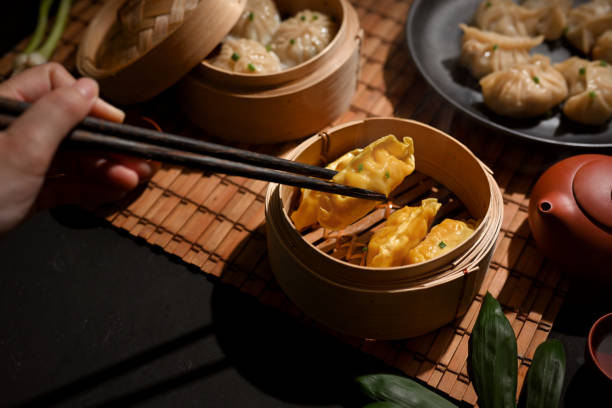 istock Female hand with chopstick picking Dimsum dumplings in bamboo steamer 1302227765