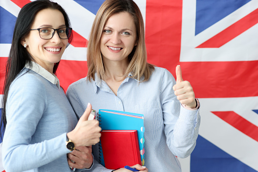 Two young women with books in hands standing against background of British flag. Learning of English language concept