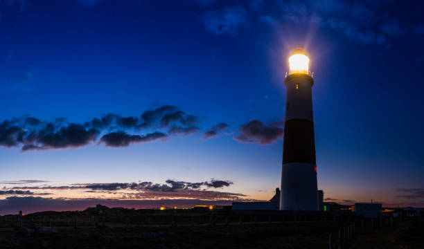 istock Lighthouse beaming out from ocean clifftop into blue dusk skies 1302233398
