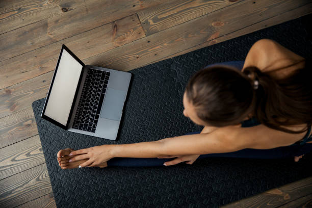 istock Female practicing yoga or pilates indoors on mat, doing exercises and stretching, watching video lesson online. Top view 1302235250