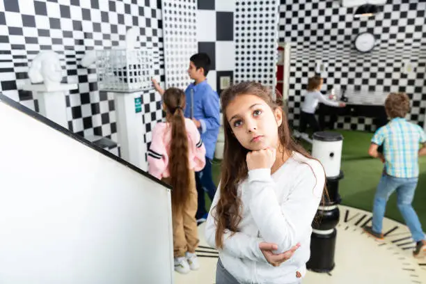 Photo of Pensive girl solving conundrum in quest room designed as chessboard