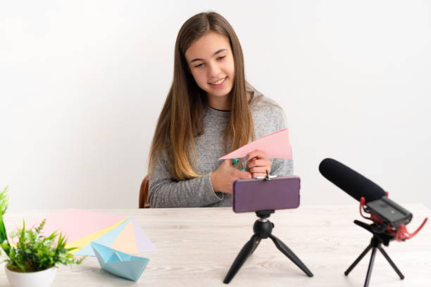 istock Woman doing doing a blog origami tutorial with colored papers looking at the camera sharing them on live social networks via internet online 1302237450