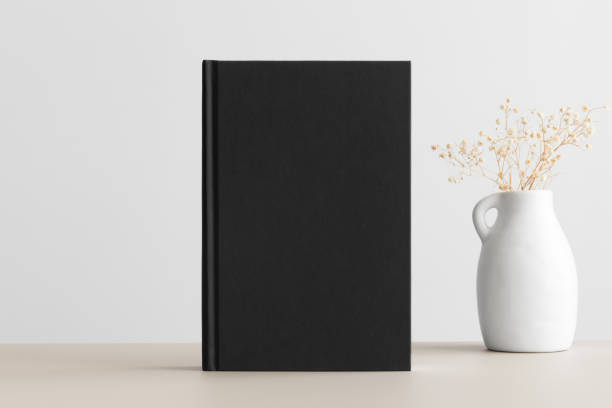 istock Black book mockup with a gypsophila decoration on a beige table. 1302239110