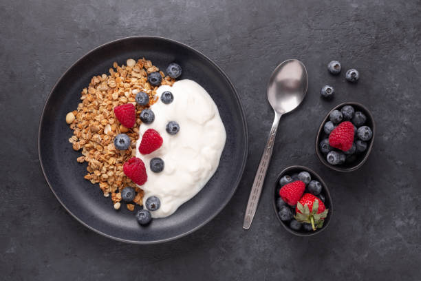 istock Yogurt with baked granola and berries in black ceramic plate on dark stone background. Healthy breakfast 1302240607