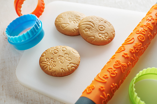 Cookies, embossing rolling pin and cookie cutters on a white cutting board