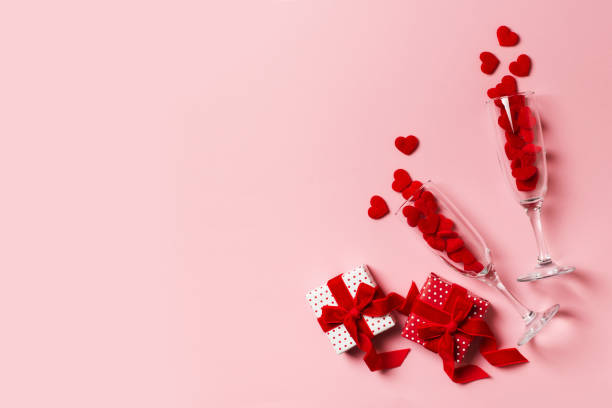 istock Two glasses with red hearts and gift flat lay on pink background 1302248596