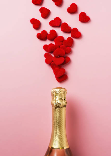 istock Chmpagne bpttle and red hearts confetti on pink background 1302248605
