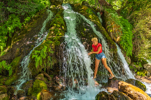 Unrecognizable energetic woman dives head first into the refreshing emerald water of a small pond in the idyllic forest. Happy female tourist cooling off in the summer by jumping into the cold stream.