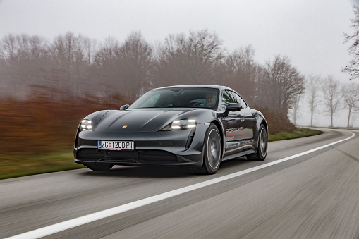 Zagreb, Croatia - December 8, 2020: Man is driving Porsche Taycan fast on the road. Taycan is all electric four door sports coupe made by famous German sports car manufacturer Porsche.
