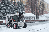 A small loader excavator bobcat removes snow from the sidewalk near the Kremlin walls during a heavy snowfall.