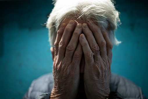 Color image depicting a senior man in his 60s in an underground subway tunnel. His expression is one of despair, sadness and depression. His hands are covering his face in a gesture of bleak desperation and hopelessness. Room for copy space.