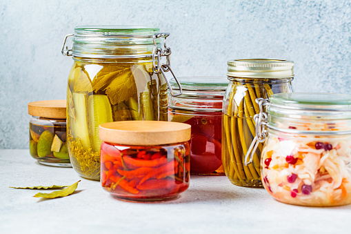 Homemade pickled or fermented vegetables - sauerkraut, wild garlic, chili, pickles, pickled tomatoes and olives in glass jars.