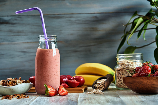 Healthy food: Banana and strawberry yogurt smoothie with cereal in bottle with straws on a rustic table.