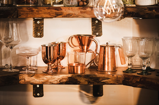 Kitchen shelves with various glass and copper glassware, mugs, tumblers and coffee utencils in beautiful daylight, horizontal composition. Interiors detail and lifestyle mood concept